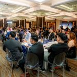 People seated at round tables in a banquet hall during a formal event or gathering.