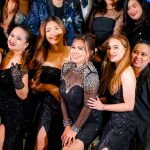 A group of people dressed in black formal attire pose and smile for a photo.