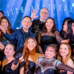 A group of people in formal attire smiling and posing at an anniversary celebration event.
