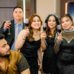 Five people dressed formally, holding wine glasses and posing for a group photo at an event.