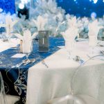 Round table set for an event with white napkins, blue runner, and table number one.