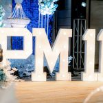 Large illuminated letters and numbers "PM11" displayed at an indoor decorated event venue.