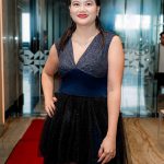 Woman in a dark blue and black dress stands on a red carpet in a modern indoor setting.