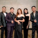 Five people dressed in formal attire pose together and smile in an indoor setting.