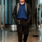 A man in business attire walks on a red carpet through glass doors.