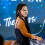 Woman in a black dress standing and smiling against a blue, star-themed backdrop.