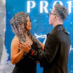 Two people in formal attire dance together at an indoor event with a blue background.