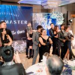 A group of people in formal attire dance together at an indoor event with festive decor.