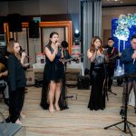 A group of musicians and singers perform indoors on a stage at an event.
