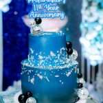 Blue two-tier cake with silver decorations and a topper reading "Profitmaster’s 11th Year Anniversary.