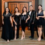 Five people in formal black attire posing together in an indoor setting.