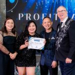 Four people pose together, one holding a certificate, at an indoor event with formal attire.