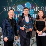 Three people in formal attire stand on stage at a "Shining Star of the Night" event.
