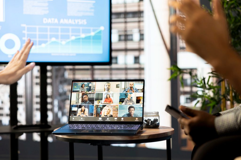 Laptop displaying a Lunch and Learn video conference; hands and multiple panels visible in foreground.