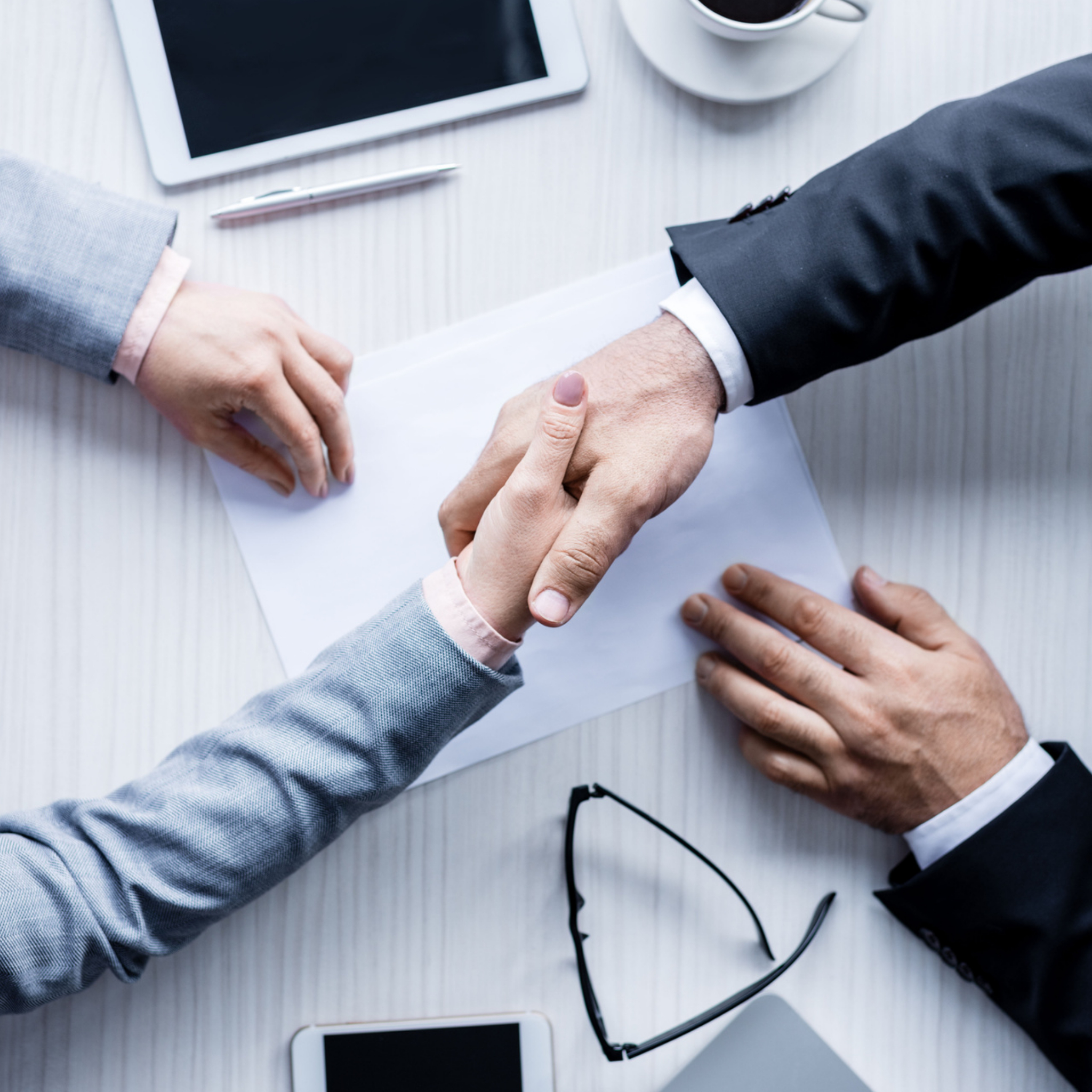 Two people in business attire shaking hands over a desk, discussing employment risks.